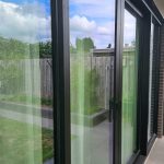 Strakke aluminium schuifpui met staallook en uitzicht op groene tuin
