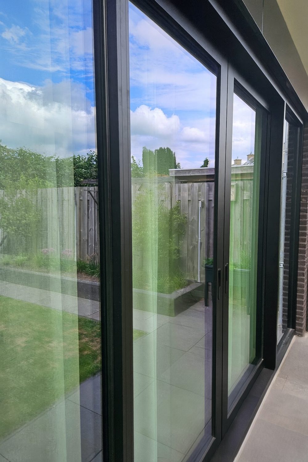 Strakke aluminium schuifpui met staallook en uitzicht op groene tuin